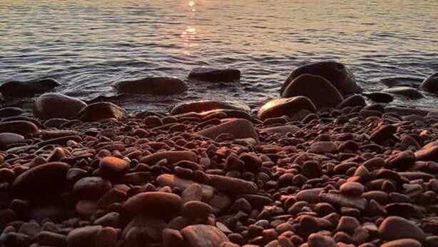 Ein Kiesstrand mit Sonnenuntergang über ruhigem Wasser.