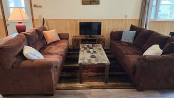 A living room with two brown sofas, a wooden coffee table, a TV, and a lamp.