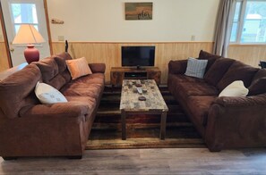 A living room with two brown sofas, a wooden coffee table, a TV, and a lamp.