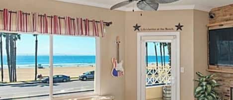 A living room with a view of the beach, a ceiling fan, and a guitar on the wall.