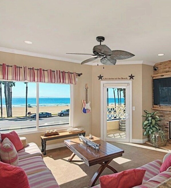 Sala de estar vista para a praia, ventilador de teto e uma guitarra na parede.