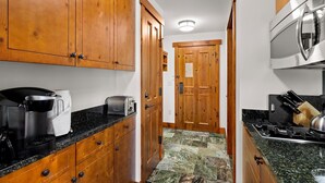 A narrow kitchen with wooden cabinets, a toaster, a coffee maker, and a stove. - Luxury Studio Ski-in Ski-Out, Hiking, Mtn Biking, Golf, Fishing (Stowe)