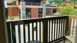 A balcony with a view of a large building with multiple windows and a stone pillar. - Luxury Studio Ski-in Ski-Out, Hiking, Mtn Biking, Golf, Fishing (Stowe)