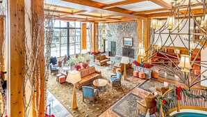 A spacious room with wooden beams, a stone fireplace, and a variety of seating arrangements. - Luxury Studio Ski-in Ski-Out, Hiking, Mtn Biking, Golf, Fishing (Stowe)