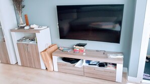 Moderni olohuone, jossa seinälle on asennettu taulutelevisio, ja huoneessa on puinen mediakeskus, jossa on kirjoja ja kaukosäädin, sekä beigenvärinen sohva.