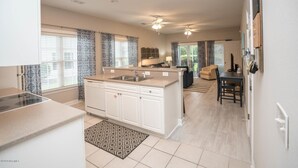 A modern kitchen with white cabinetry, a central island, and a dining area with a table and chairs. - Nautical Living with a touch of Golf (3701) (Sunset Beach)