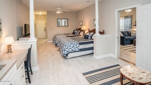 A bedroom with a large bed, a desk, and a chair. There is a ceiling fan and a door leading to another room. - Nautical Living with a touch of Golf (3701) (Sunset Beach)