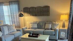 A living room with a sofa, a coffee table, a lamp, and a patterned rug. - Nautical Living with a touch of Golf (3701) (Sunset Beach)
