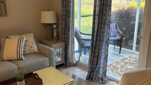 A living room with a sofa, a coffee table, a lamp, and a view of the outdoors through a sliding glass door. - Nautical Living with a touch of Golf (3701) (Sunset Beach)
