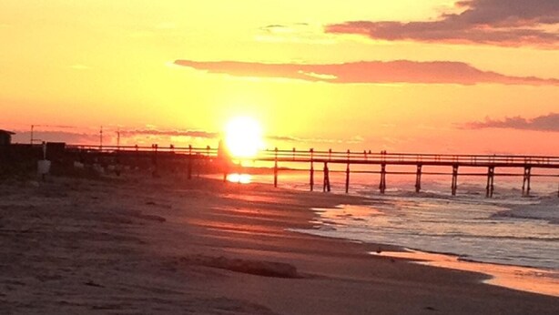 A beach with a pier extending into the ocean during sunset. - Nautical Living with a touch of Golf (3701) (Sunset Beach)