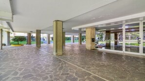Ein geräumiger überdachter Bereich mit Steinböden, Betonpfeilern und Glastüren zu einem Innenraum.