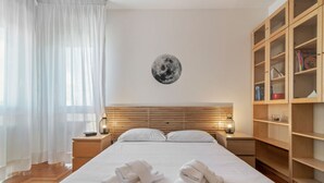 Ein Hotelzimmer mit einem großen Bett, zwei Nachttischen, einem Holzkopfstück, einem Wandgemälde mit einem Mondmotiv, einem großen Fenster mit transparenten Vorhängen und einem Holzregal.