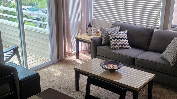 A cozy living room with a sofa, coffee table, and a dining area with a table set for two. - Cozy 2 bed 2 bath in Arcadian Dunes (Myrtle Beach)