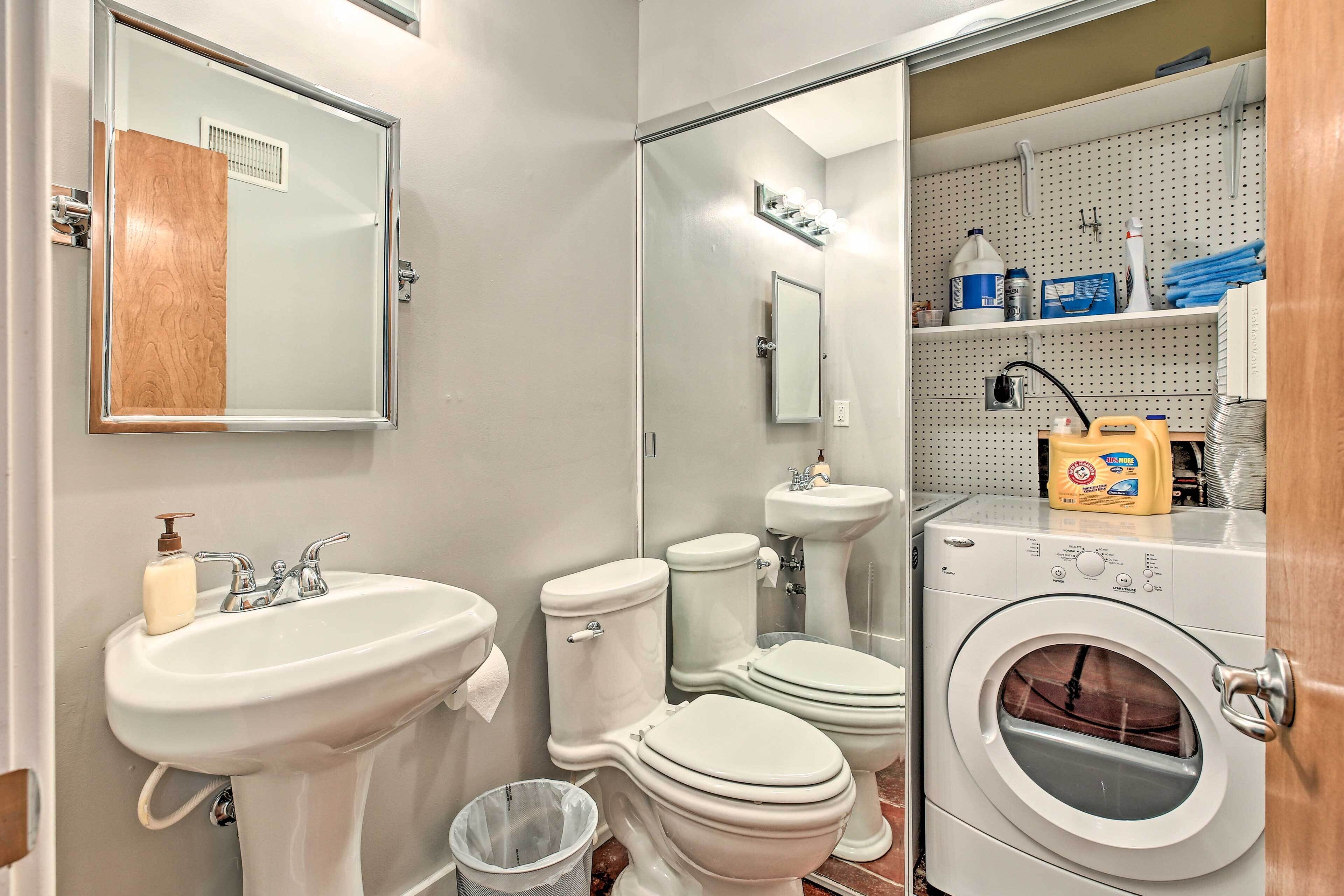 A compact bathroom with a sink, two toilets, a mirror, and a washing machine.