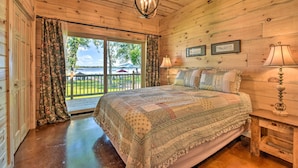 A wooden cabin bedroom with a large bed, a chandelier, and a view of the outdoors. - Spacious Pearl Lake Retreat w/ Yard & Private Dock (Kimball)