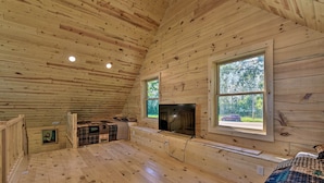 A cabin with wooden walls and floors, a fireplace, a large window, and a staircase. - Spacious Pearl Lake Retreat w/ Yard & Private Dock (Kimball)