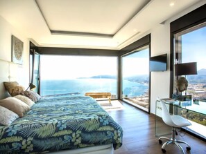 Ein Schlafzimmer mit einem großen Bett, einem Schreibtisch mit Stuhl und Blick auf das Meer.