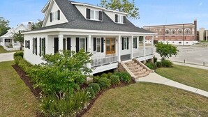 Uma casa térrea com telhado em duas águas, varanda frontal e pequeno jardim com paisagismo.