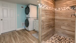 A laundry room with a washing machine, dryer, and a shower area with wooden walls and a tiled floor. - Riverview cottage (Grant-Valkaria)