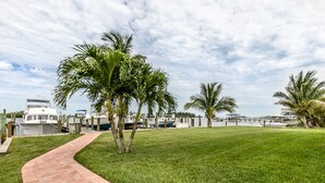 A pathway leading to a waterfront area with boats, palm trees, and a clear sky. - Riverview cottage (Grant-Valkaria)