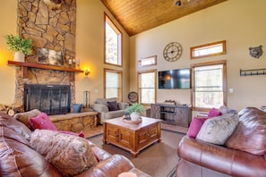 A spacious living room with a stone fireplace, leather sofas, a wooden coffee table, and a television.