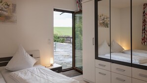 A bedroom with a bed, bedside table, and a wardrobe. There is a window with a view of a garden. - Eifelnatur (Haus 1) by Interhome (Immerath)