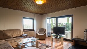 A modern living room with a sofa, armchair, glass coffee table, and a TV on a stand. - Eifelnatur (Haus 1) by Interhome (Immerath)