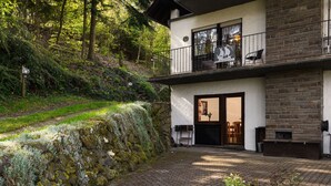 A two-story house with a stone facade, a balcony with outdoor seating, and a stone retaining wall. - Eifelnatur (Haus 1) by Interhome (Immerath)