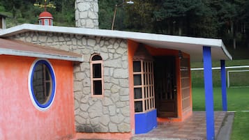 Un pequeño edificio colorido con fachada de piedra, techo rojo y puerta azul.