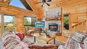 Interior acogedor de una cabaña con chimenea de piedra, paredes de madera, un televisor y un área de estar confortable.