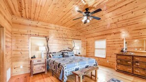 Un dormitorio de cabaña de madera con cama, mesita de noche, cómoda y ventilador de techo.