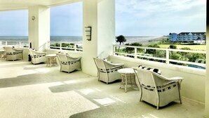 Un espace extérieur abrité, aménagé avec des meubles en osier et offrant une vue sur la plage et l’océan.