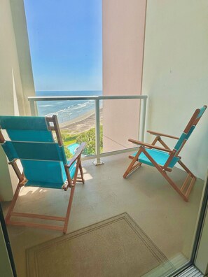 A balcony with two wooden folding chairs and a view of the ocean.
