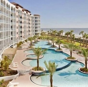 Enjoy a scenic view of the ocean from your room, with easy access to the beach and a relaxing pool area featuring interconnected pools and palm trees.