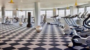 Une salle de sport avec un sol à carreaux noirs et blancs, des tapis de course, des appareils de musculation elliptiques et des poids libres.