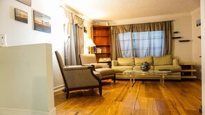 Una sala de estar con piso de madera, un sofá, un sillón, una mesa de centro y una estantería.