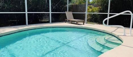 En pool med kristallklart vatten, en vit poolterrass och en solstol.