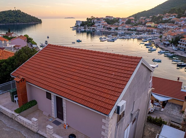 A coastal town with a prominent building featuring a red-tiled roof, situated near a marina with numerous boats.