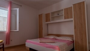 A bedroom with a bed, wooden flooring, a window with curtains, and built-in wooden shelving. - Apartments Peselj-Three Bedroom Apartment with Terrace and Sea View (Smokvica)