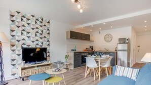 A modern living room with a TV, a sofa, and a dining area with chairs and a table. - Les Gemeaux by Interhome (Quiberon)
