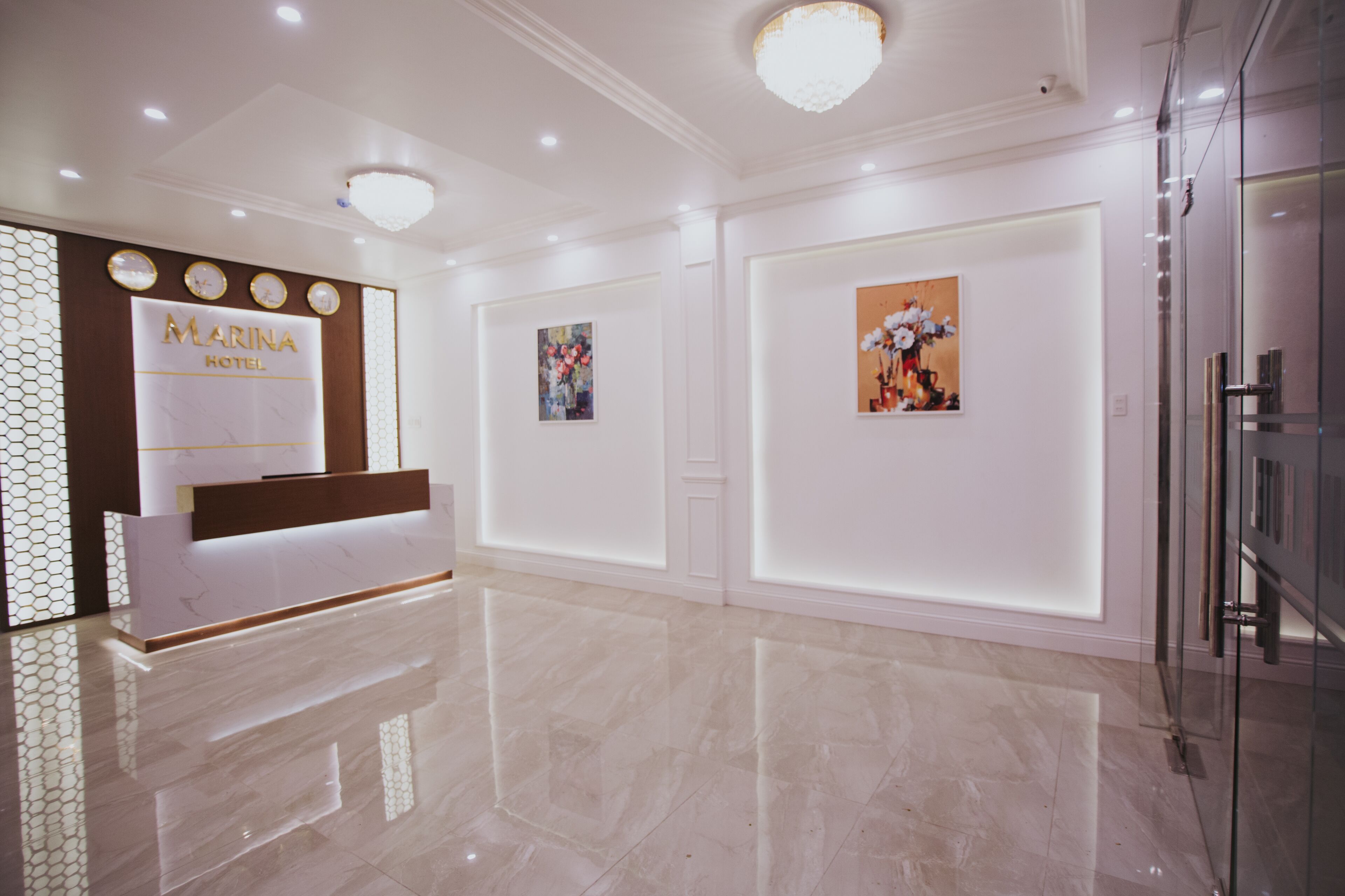 Zona de recepción de un hotel, con suelo de mármol, mostrador de recepción y relojes en la pared.