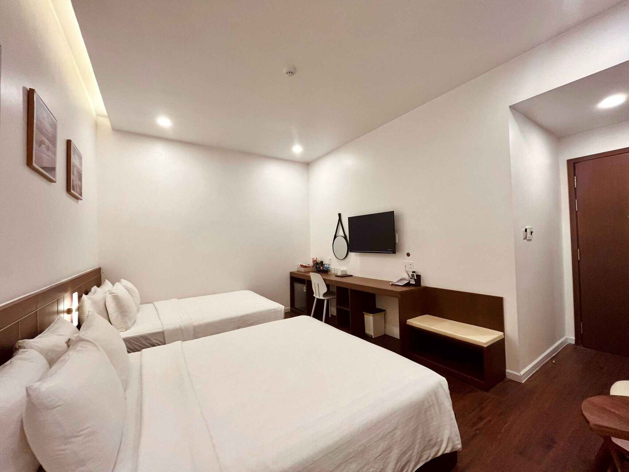 A hotel room with two beds, a desk, a TV, and a door.