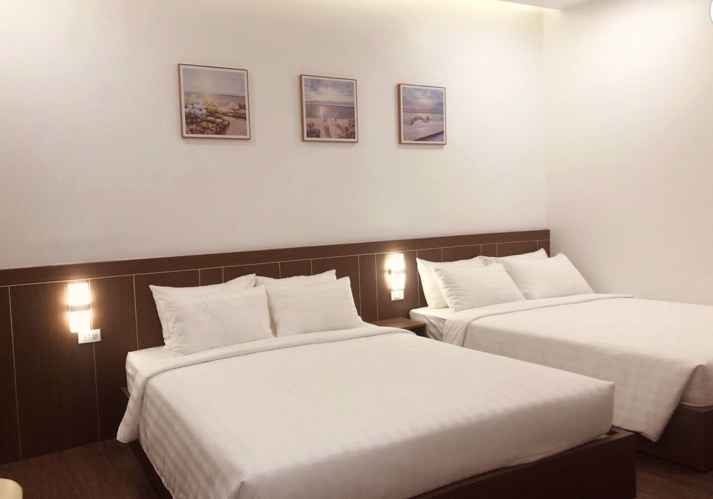 A hotel room with two beds, a wooden headboard, and three framed pictures on the wall.
