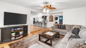 Ein Wohnzimmer mit Flachbildfernseher, dunklem Holz-Entertainment-Center, Deckenventilator, Ecksofa und Couchtisch.