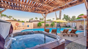 Ein Whirlpool unter einer Holzpergola, ein Schwimmbecken und Liegestühle.