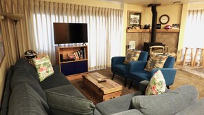 Een woonkamer met een bank, fauteuils, een salontafel, een televisie en een open haard.