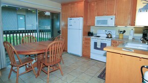 Een keuken met houten kastjes, een koelkast, een magnetron, een oven en een eettafel met stoelen.