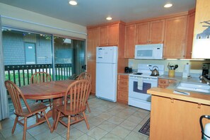 Kitchen area with a stove, microwave, and kettle, adjacent to a dining space with a table and chairs.