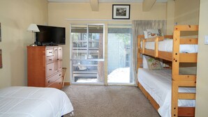 Een slaapkamer met een televisie, een dressoir, een stapelbed en een schuifdeur die leidt naar een balkon.