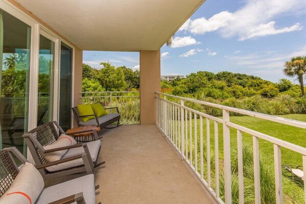 Un balcon doté de mobilier d’extérieur, d’une balustrade blanche et offrant une vue sur une végétation luxuriante et des arbres.